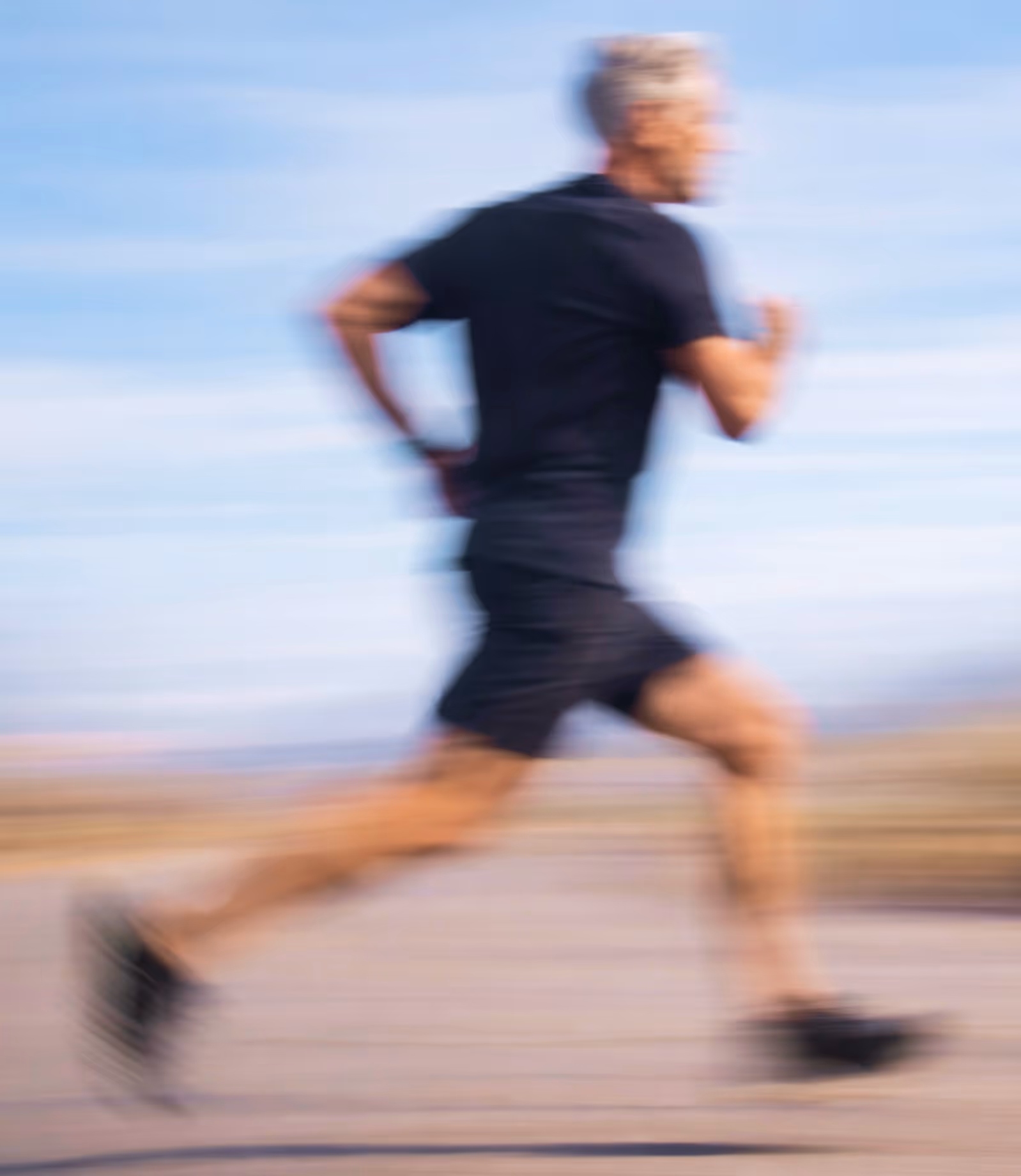 Older man with gray hair running outdoors at speed, motion-blurred against a blue sky.
